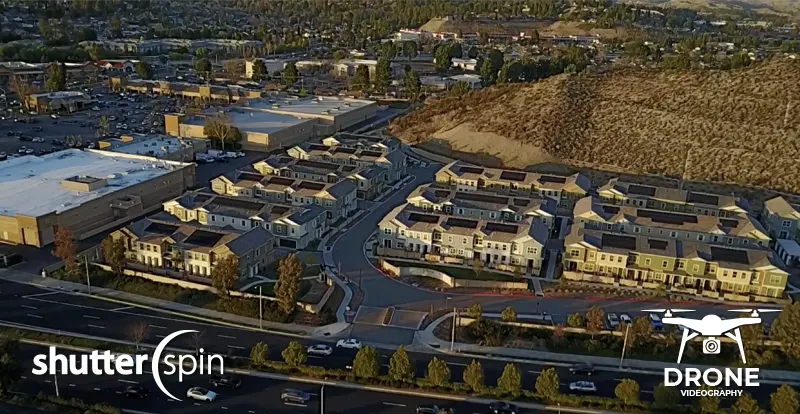 Drone aerial view of a modern subdivision and surrounding community, captured by ShutterSpin. Wide-angle drone photography highlights neighborhood context, shopping, and amenities for real estate marketing.
